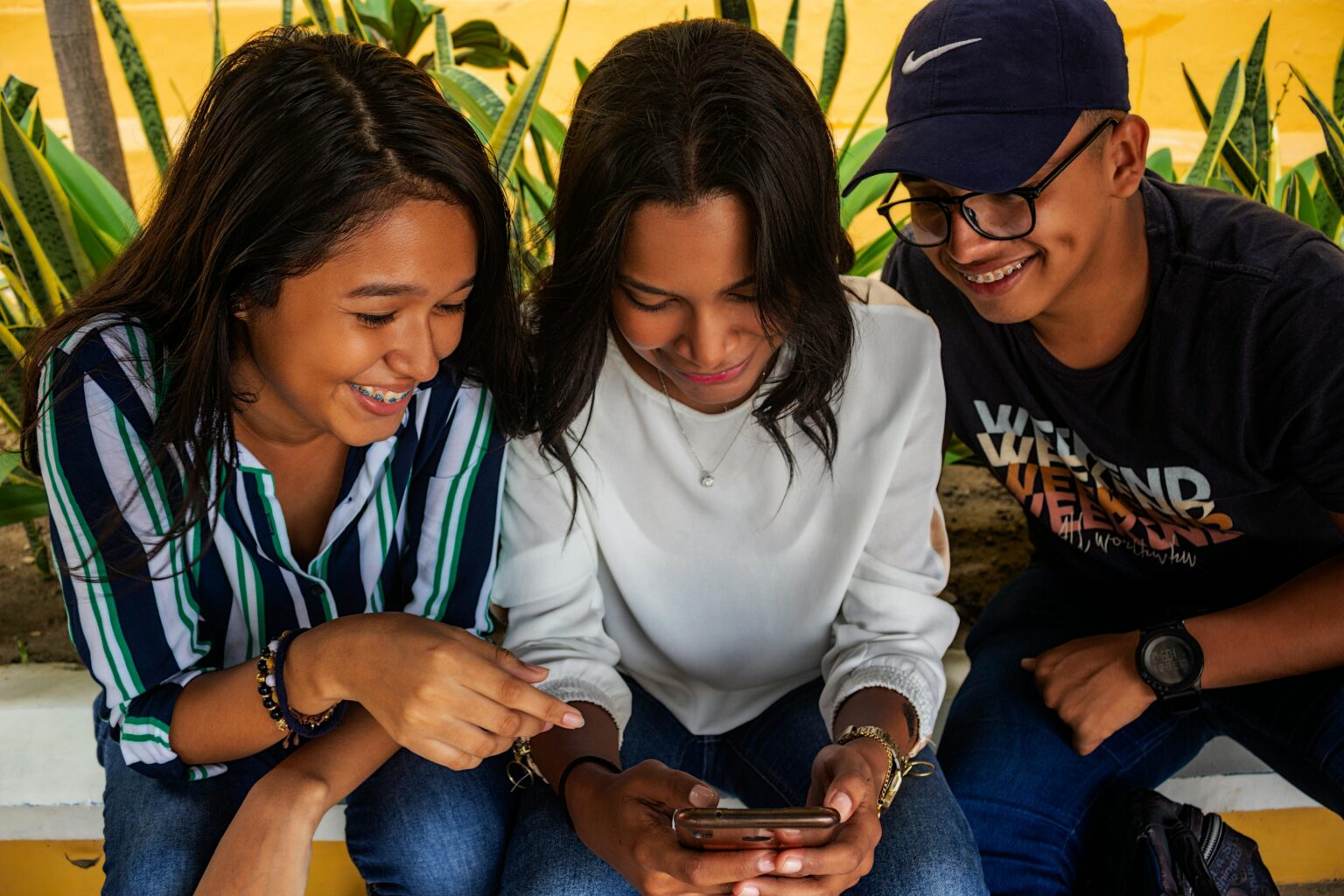 Three young friends in Barranquilla share a moment around a smartphone, smiling and bonding.